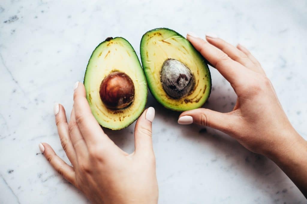 Woman holding open a cut up avocado on the table - surprising food to eat when craving sugar