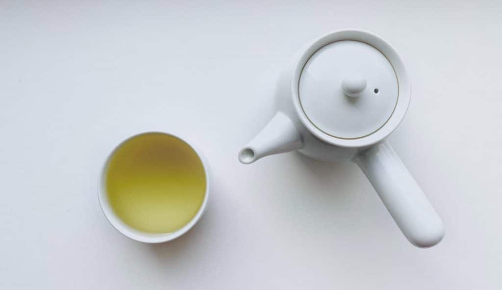 Green tea in a cup with a tea pot on a tabletop 