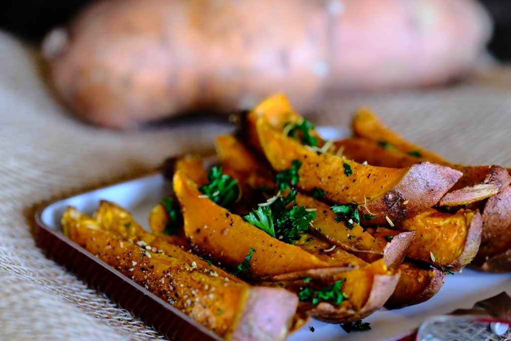 Sliced baked sweet potato fries on a baking sheet with chopped parsley over the top