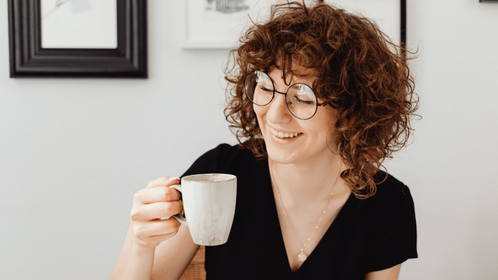 woman smiling hold a coffee cup in one hand and wearing a v neck shirt to help reduce broad shoulders 
